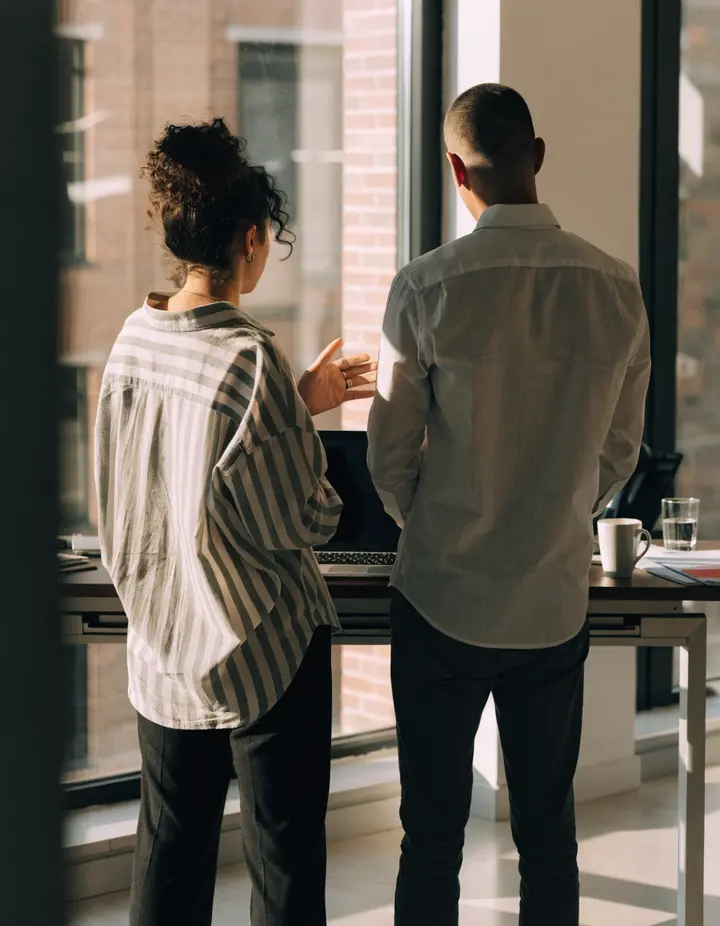 Two people talking at a standing desk by a window