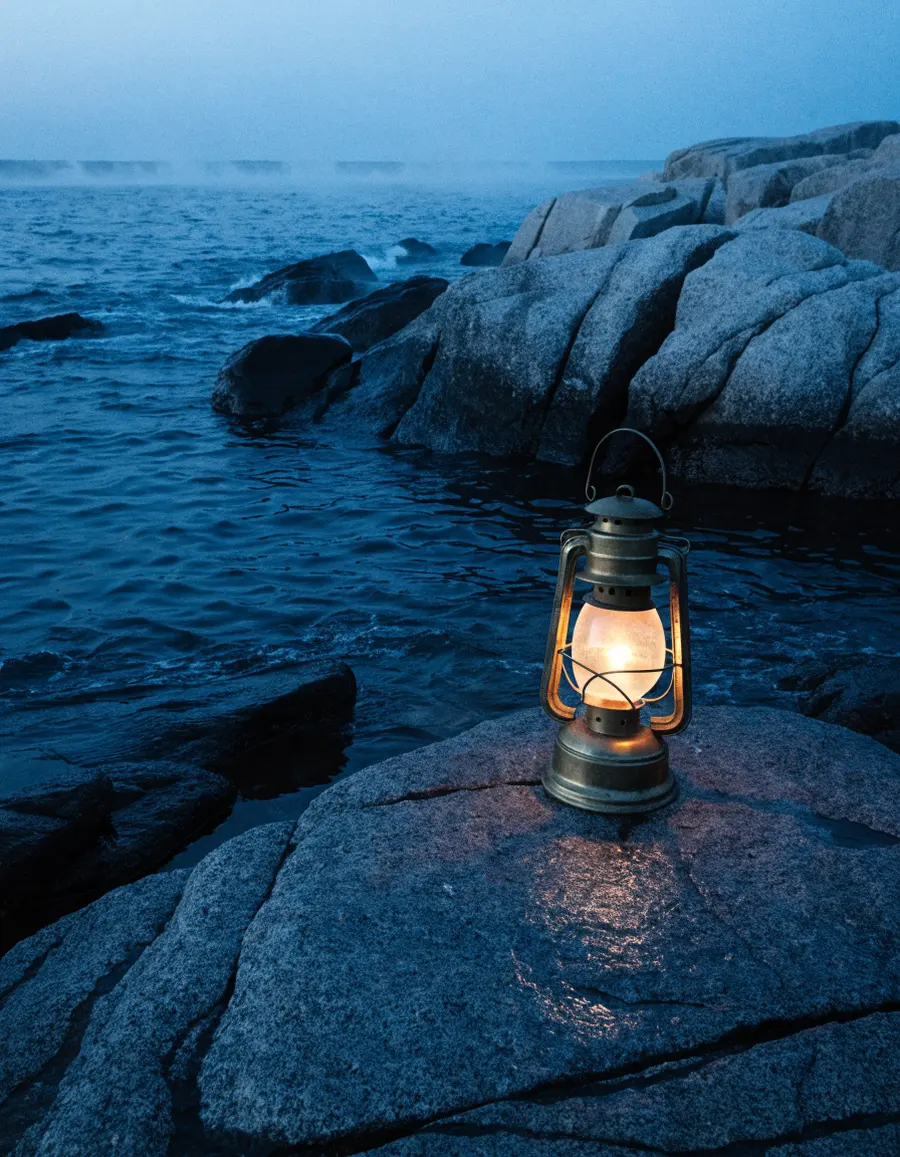 A lit storm lantern on wet granite rocks by the sea at dusk