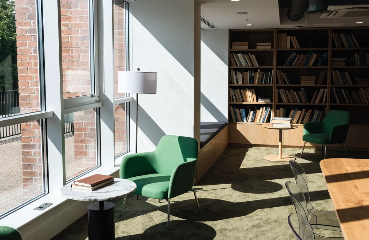 A bright coworking lounge with green armchairs and bookshelves