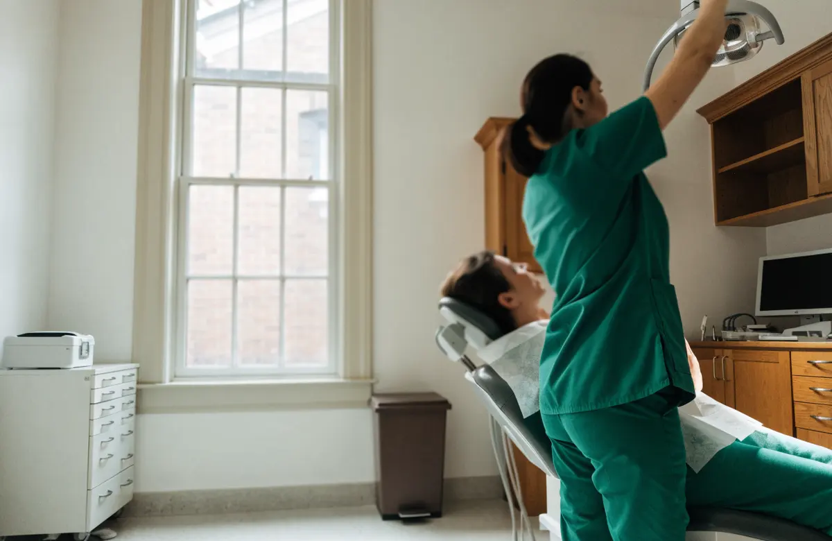 A hygienist adjusts the overhead light beside a reclined patient
