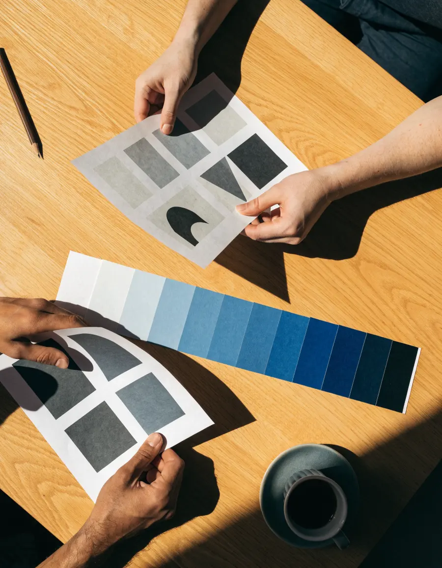 Two people reviewing printed design proofs and a swatch fan on a wooden table