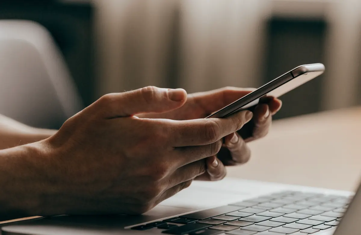 Hands holding a phone with a sign-in code prompt beside a laptop