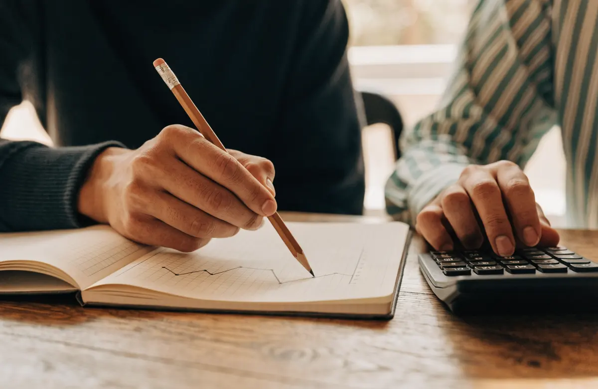Two people at a table, one pointing a pencil at a graph in a notebook