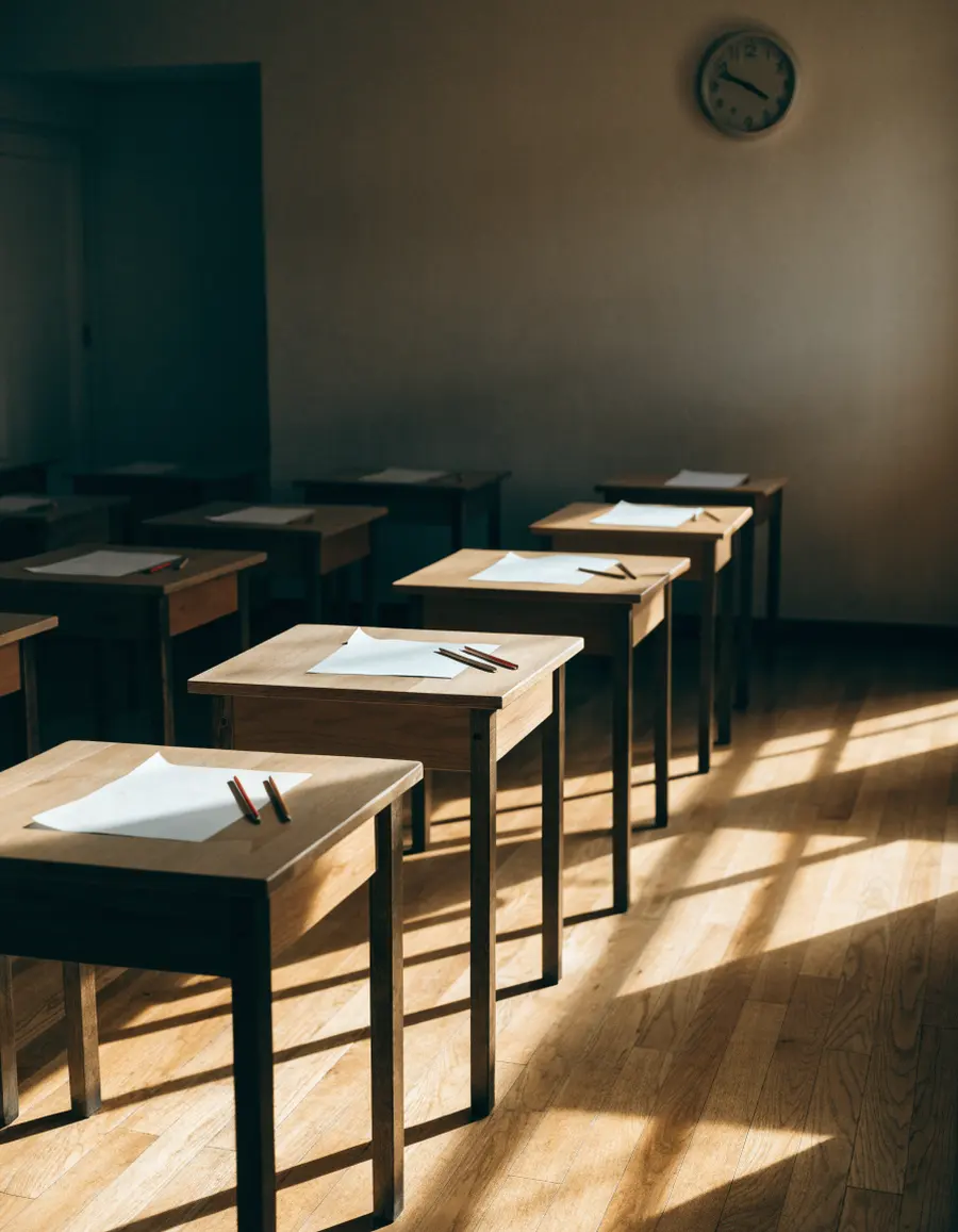 Rows of empty desks with pencils laid out in a quiet, sunlit room on a Saturday morning